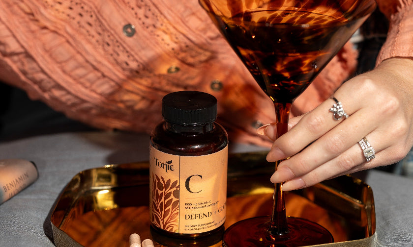 Person pouring a drink into a martini glass with a bottle of 'C' vitamins on a tray.